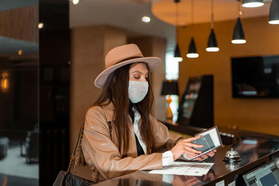 Melhor transfer em Nova York com motorista brasileiro 5 Woman wearing mask and hat checking in at hotel front desk, symbolizing travel and safety.
